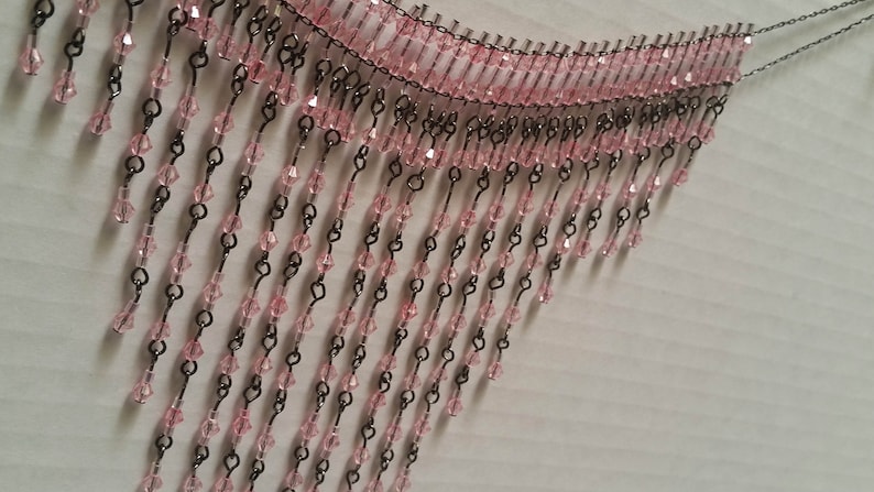 Pode incluir: Uma guarni&ccedil;&atilde;o de franja de contas cor-de-rosa com elos de corrente de metal preto. A franja &eacute; feita de pequenas contas facetadas que pendem da corrente.