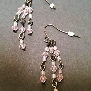Pode incluir: Um par de brincos pendentes com contas de cristal rosa e detalhes em metal prateado.