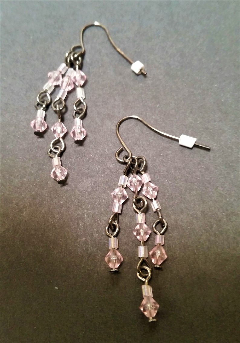 Pode incluir: Um par de brincos pendentes com contas de cristal rosa e detalhes em metal prateado.