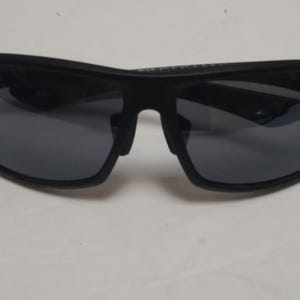 May include: Black sunglasses with dark gray lenses. The sunglasses have a thick, curved frame and a bridge over the nose. The lenses are reflective, and the sunglasses appear to be made of plastic.