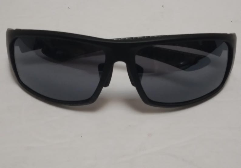 May include: Black sunglasses with dark gray lenses. The sunglasses have a thick, curved frame and a bridge over the nose. The lenses are reflective, and the sunglasses appear to be made of plastic.
