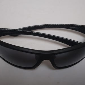 May include: Black sunglasses with a matte finish and dark lenses. The arms have a textured pattern. These sunglasses are designed for sports and outdoor activities.