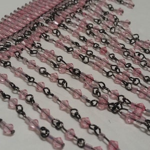 Pode incluir: Franja de contas rosa e preta. A franja &eacute; feita de pequenas contas facetadas enfiadas em um fio fino. As contas s&atilde;o rosa e o fio &eacute; preto.
