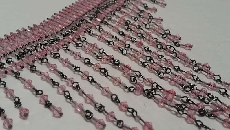 Pode incluir: Franja de contas rosa e preta. A franja &eacute; feita de pequenas contas facetadas enfiadas em um fio fino. As contas s&atilde;o rosa e o fio &eacute; preto.
