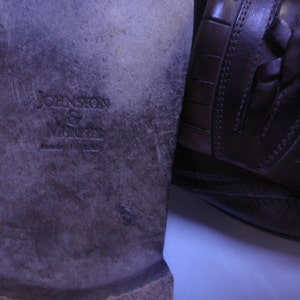 Puede incluir: Primer plano de la suela de un mocas&iacute;n de cuero marr&oacute;n con el texto "Johnston & Murphy" grabado en la parte inferior.