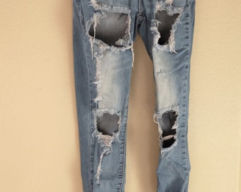 May include: Distressed light blue denim jeans with several rips and tears throughout the legs. The jeans have a high rise and a skinny fit. The waistband has the text "S.O.N.G. CURVY HIGH RISE" printed on it.