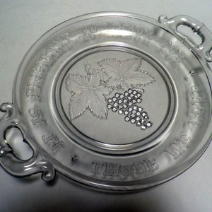 May include: Clear glass serving plate with two handles and a raised grape and leaf design in the center. The plate has the words "IT IS PLEASANT TO LABOR FOR THOSE WE LOVE" etched around the rim.