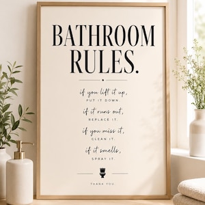May include: A framed print with the text "BATHROOM RULES" in black. The rules include "if you lift it up, put it down" and "if it smells, spray it." The print is in a light wood frame and is displayed in a bathroom setting.