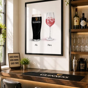 May include: A framed print featuring a pint of Guinness and a glass of pink cocktail, labeled "His" and "Hers." The bar scene includes a Guinness bar mat, a sign that says "Good Friends Good Drinks Good Times," and a shelf with liquor bottles.