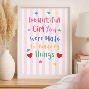 May include: A framed print with the words "Beautiful Girl You Were Made For Amazing Things" in colorful text on a pink striped background. The print is decorated with stars and hearts. The text "This belongs on her wall" is at the bottom.