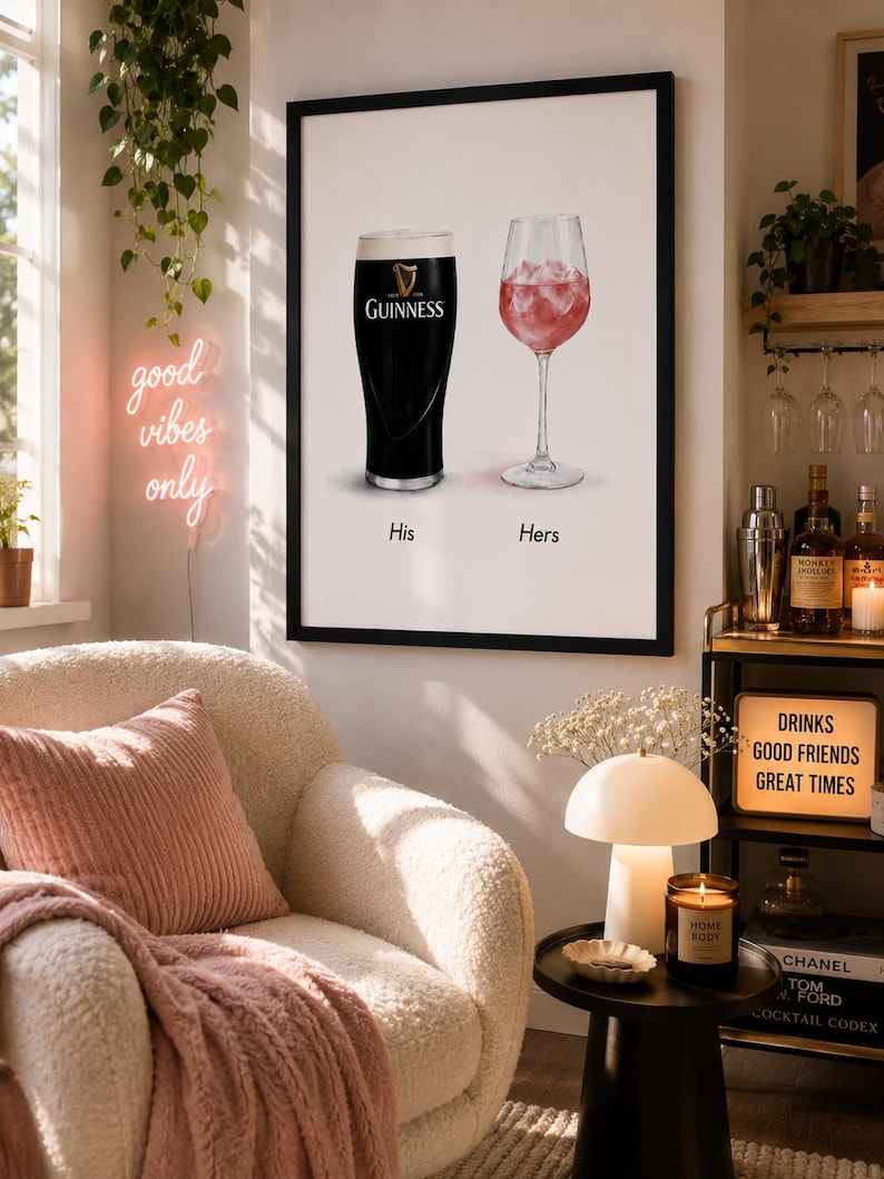 May include: A framed print featuring a pint of Guinness and a glass of ros&eacute;, labeled "His" and "Hers." The print hangs above a cozy armchair with a pink pillow and blanket. A neon sign reads "good vibes only."