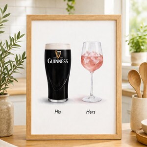 May include: Framed print featuring a pint of Guinness and a glass of pink drink with ice. The Guinness glass has the brand logo. Text below reads "His" and "Hers". The print is in a wooden frame.
