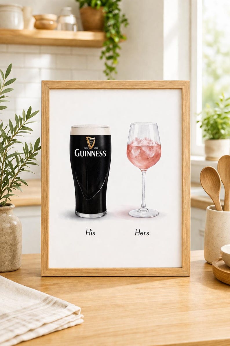 May include: Framed print featuring a pint of Guinness and a glass of pink drink with ice. The Guinness glass has the brand logo. Text below reads "His" and "Hers". The print is in a wooden frame.
