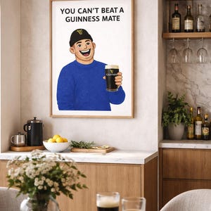 Peut inclure: Impression encadr&eacute;e avec l'inscription &laquo; YOU CAN'T BEAT A GUINNESS MATE &raquo; au-dessus d'une illustration d'un homme tenant une pinte de Guinness. L'image est dans une cuisine avec une table, des fleurs et des boissons, dont deux pintes de bi&egrave;re.