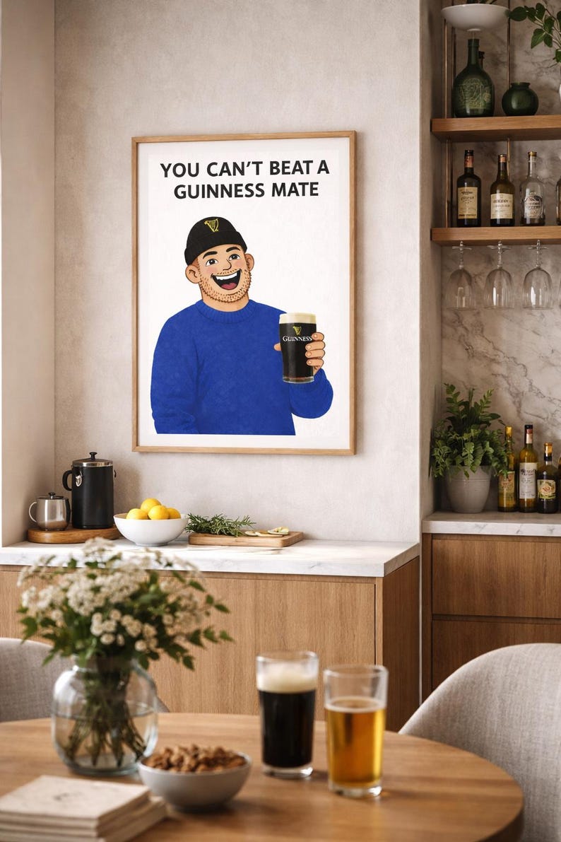 Peut inclure: Impression encadr&eacute;e avec l'inscription &laquo; YOU CAN'T BEAT A GUINNESS MATE &raquo; au-dessus d'une illustration d'un homme tenant une pinte de Guinness. L'image est dans une cuisine avec une table, des fleurs et des boissons, dont deux pintes de bi&egrave;re.