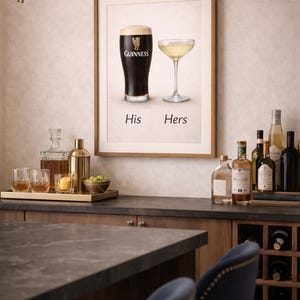 Może przedstawiać: Oprawiony wydruk przedstawiający kufel Guinnessa i kieliszek do szampana z napisem "His Hers". Obraz wyświetlany jest nad barem z butelkami alkoholi i win. Na barze znajduje się taca ze szklankami i shakerem do koktajli.