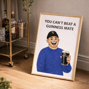 Peut inclure: Impression encadr&eacute;e en bois avec une illustration de dessin anim&eacute; d'un homme tenant une pinte de Guinness. L'homme porte un pull bleu et un bonnet noir. Le texte "YOU CAN'T BEAT A GUINNESS MATE" est affich&eacute;.