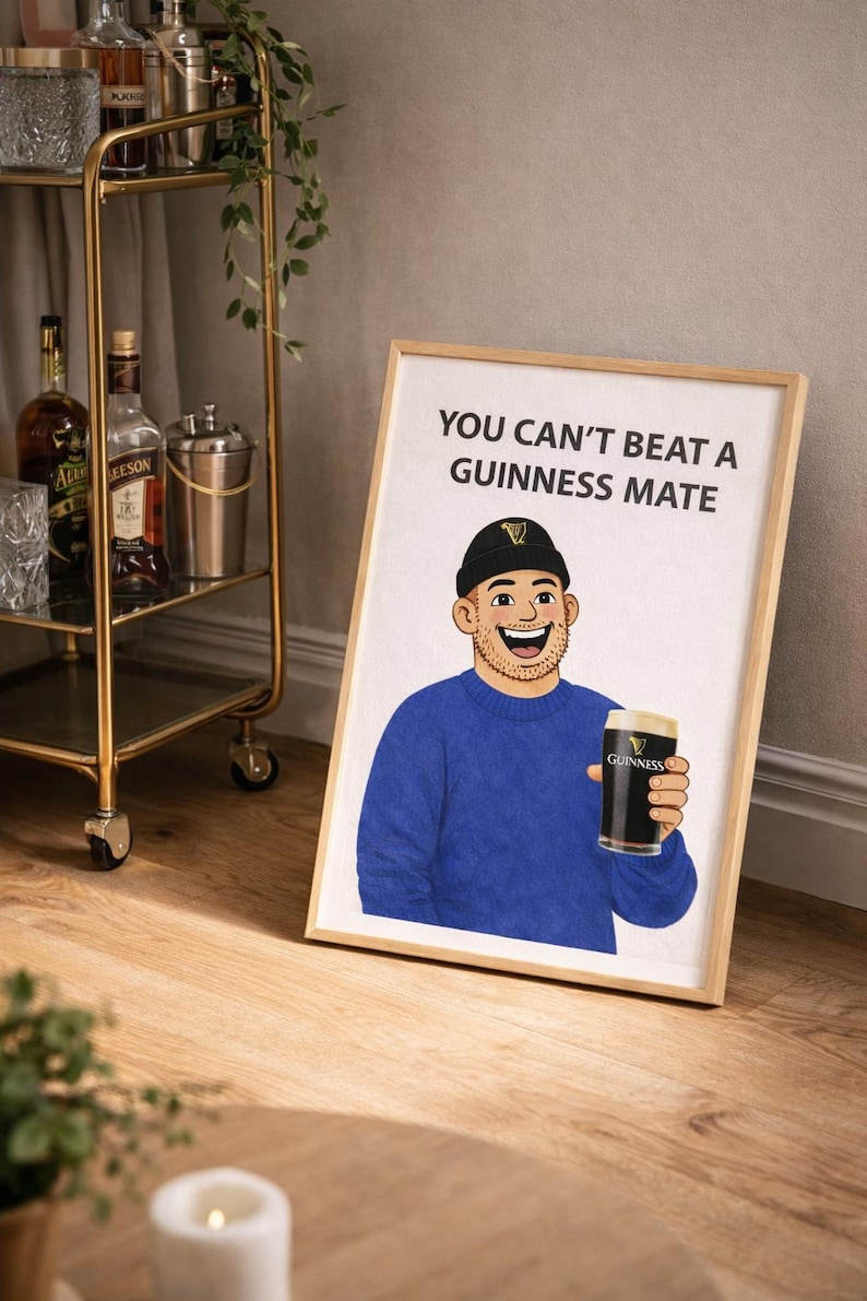 Peut inclure: Impression encadr&eacute;e en bois avec une illustration de dessin anim&eacute; d'un homme tenant une pinte de Guinness. L'homme porte un pull bleu et un bonnet noir. Le texte "YOU CAN'T BEAT A GUINNESS MATE" est affich&eacute;.