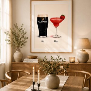 May include: A framed print featuring a pint of Guinness and a red cocktail with a strawberry garnish. The words "His" and "Hers" are below the drinks. The print is displayed in a dining room setting.