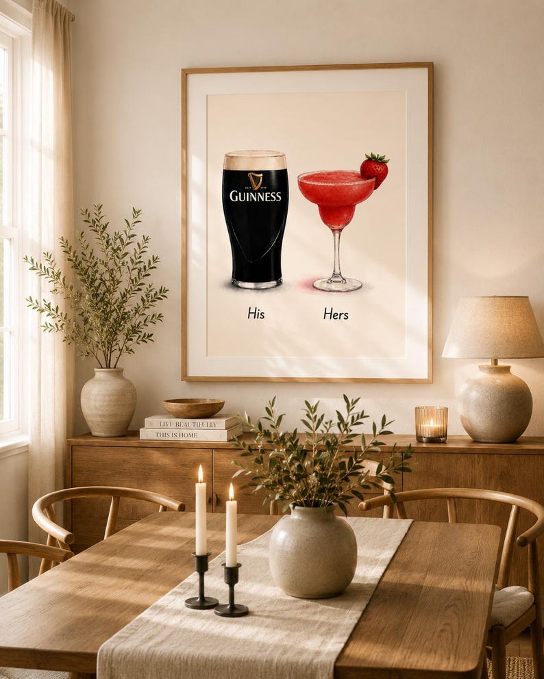 May include: A framed print featuring a pint of Guinness and a red cocktail with a strawberry garnish. The words "His" and "Hers" are below the drinks. The print is displayed in a dining room setting.