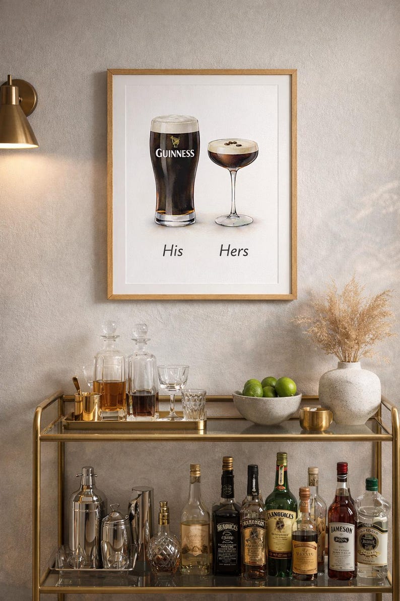 Puede incluir: Un cuadro enmarcado con una pinta de Guinness y un c&oacute;ctel, etiquetados como "His" y "Hers". La imagen est&aacute; sobre un carrito de bar dorado con varias botellas, copas y un cuenco con limas. Tambi&eacute;n hay un jarr&oacute;n decorativo con flores secas.
