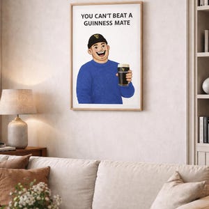 Peut inclure: Impression encadr&eacute;e avec une illustration de dessin anim&eacute; d'une personne tenant une pinte de Guinness. La personne porte un pull bleu et un bonnet noir. Le texte "YOU CAN'T BEAT A GUINNESS MATE" est affich&eacute; au-dessus de l'illustration. L'&oelig;uvre est expos&eacute;e dans un salon.