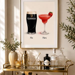 May include: A framed print featuring a pint of Guinness and a strawberry margarita, labeled "His" and "Hers." The print is displayed above a gold bar cart with bottles of liquor, glassware, and bar tools. The overall theme is home bar decor.