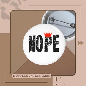 Könnte beinhalten: Ein weißer Button mit dem Wort "NOPE" in verblichener schwarzer Schrift, gekrönt von einer roten Krone. Der Button befindet sich vor einem neutralen Hintergrund mit dem Text "MORE DESIGNS AVAILABLE".