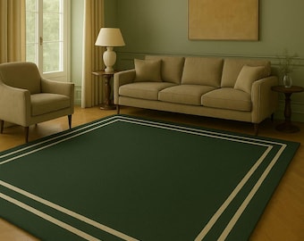 May include: A dark green rectangular rug with a double cream border, placed on a light brown hardwood floor. The rug is the focal point of a living room, with a sofa, armchair, and a window with cream curtains in the background.