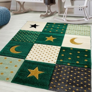 Puede incluir: Una colorida alfombra con diseño de patchwork. La alfombra presenta cuadrados verdes, crema y grises, adornados con estrellas, lunas y lunares dorados y negros. La alfombra está diseñada para una habitación infantil.