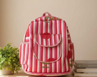 May include: A pink and white striped backpack with a front pocket and side pockets. The backpack has a top handle and adjustable straps. The design includes floral accents. The backpack is sitting on a wooden table.