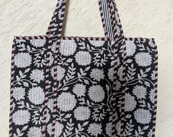 Può includere: Borsa tote nera con motivo floreale bianco. La borsa ha una forma rettangolare con un design floreale in bianco e nero. I manici sono neri con strisce bianche e rosa. Un accessorio elegante e pratico.