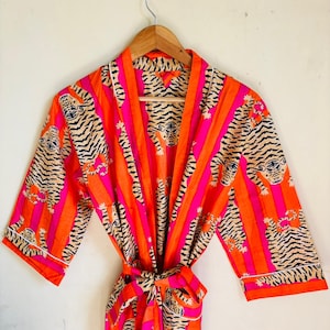 May include: A vibrant, open-front robe with a tiger print. The robe features a repeating pattern of tigers in black and tan against a background of vertical stripes in bright orange and pink. The robe has a matching tie belt.