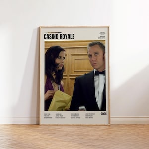 May include: A framed movie poster for "Casino Royale" featuring Daniel Craig and Eva Green. The poster has a beige background with the movie title at the top. The actors are in the center, with the year 2006 at the bottom right.