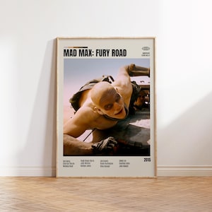 May include: A framed movie poster for "Mad Max: Fury Road" featuring a bald character leaning out of a vehicle. The poster has a beige background with the movie title and credits. The year 2015 is also visible.