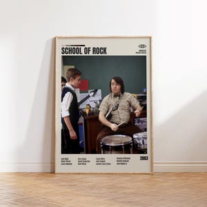 May include: A framed movie poster for "School of Rock" featuring Jack Black playing drums. The poster has a beige background with the movie title at the top and the year 2003. The cast and crew are listed at the bottom.
