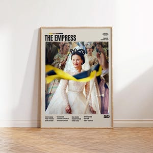 以下が含まれることがあります： 映画「The Empress」のフレーム入りポスター。白いガウンとベールを着た女性が黒いヘッドピースを着用しています。ポスターはベージュの背景に映画のタイトルとクレジットがあります。