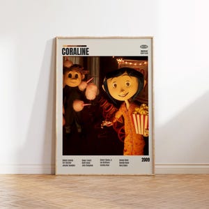 May include: A framed movie poster for the animated film "Coraline" featuring the title and the year 2009. The poster shows two characters, one holding popcorn and the other holding cotton candy. The poster is in a wooden frame.