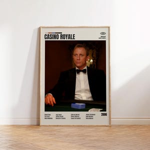 May include: A framed movie poster for "Casino Royale" featuring Daniel Craig in a tuxedo. The poster has a beige background with the movie title in bold black letters. The poster includes the year 2006 and the names of the actors.