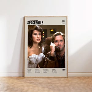 May include: A framed movie poster for the 1987 film "Spaceballs." The poster features two actors, a woman in a white dress and a man on the phone. The title is at the top, with the year at the bottom.