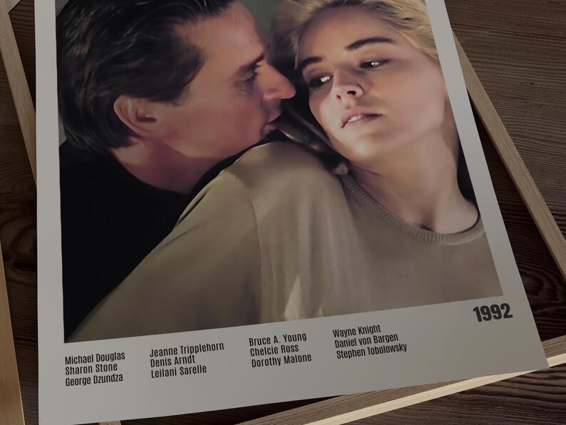 May include: A framed movie poster featuring Michael Douglas and Sharon Stone. The poster has a close-up of the actors, with text at the bottom listing the cast and the year 1992.