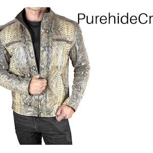 Może przedstawiać: Skórzana kurtka ze wzorem skóry węża, zapinana na zamek błyskawiczny i z dwiema kieszeniami na piersi. Kurtka ma brązowy kołnierz i jest noszona na czarnej koszulce i ciemnych dżinsach. Tekst "PurehideCrafts" jest widoczny w prawym górnym rogu.