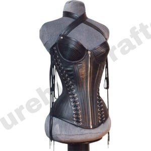 May include: Black leather corset with a halter neck and vertical ribbing. The corset features a front zipper closure and lace-up detailing on the sides. The garment is displayed on a gray mannequin.