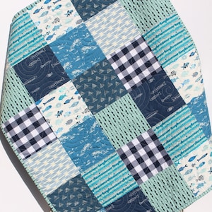 May include: A blue and white patchwork baby quilt with a variety of patterns, including fish, geometric shapes, and stripes.