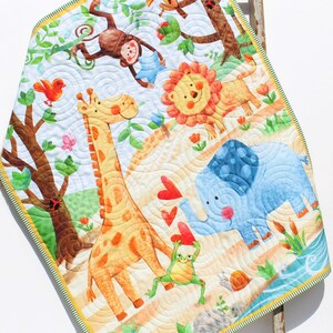 May include: A colorful baby quilt with a jungle theme. The quilt features a giraffe, elephant, monkey, lion, frog, and toucan. The background is a light blue with white swirls.