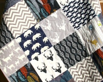 May include: A patchwork quilt with a variety of patterns, including deer, bears, feathers, and geometric designs. The quilt is made in shades of gray, black, and white.