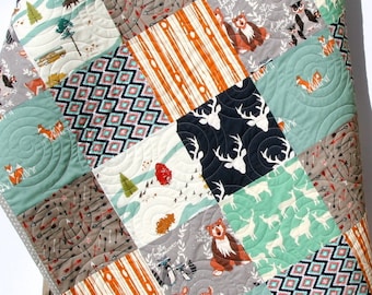 May include: A patchwork baby quilt with a woodland theme. The quilt is made of various fabrics with different patterns, including deer, foxes, bears, and arrows. The quilt is in shades of green, brown, black, and white.