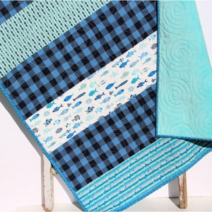 May include: A blue and white baby quilt with a checkered pattern, a fish print, and a solid blue backing. The quilt is made with cotton fabric and is perfect for a nursery or child's room.