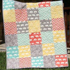 May include: A patchwork baby quilt with a variety of patterns, including elephants, bicycles, and chevron stripes. The quilt is made in shades of gray, yellow, teal, and coral.