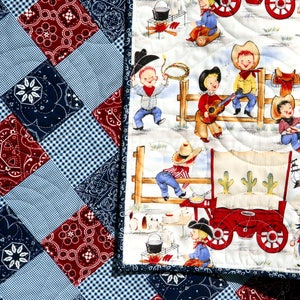May include: A white and blue patchwork quilt with a red, white, and blue bandana print. The quilt features a scene of cowboys and a wagon on a white background.